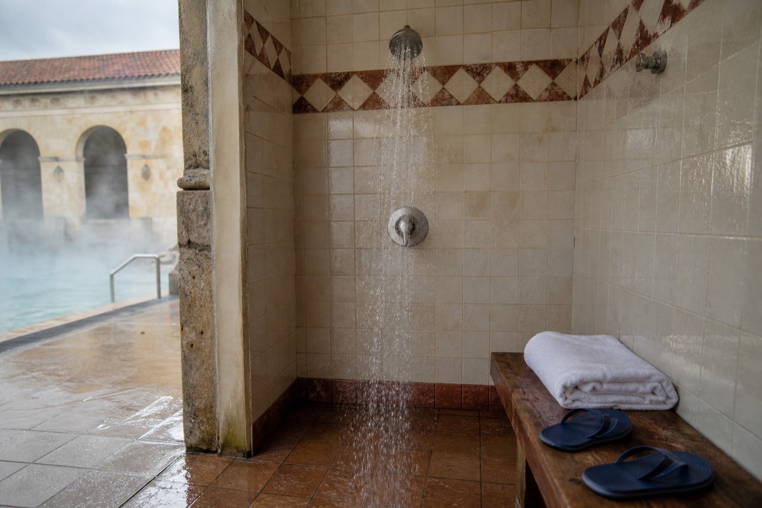 Poolside shower area with flip-flops and towels at a Budapest thermal bath