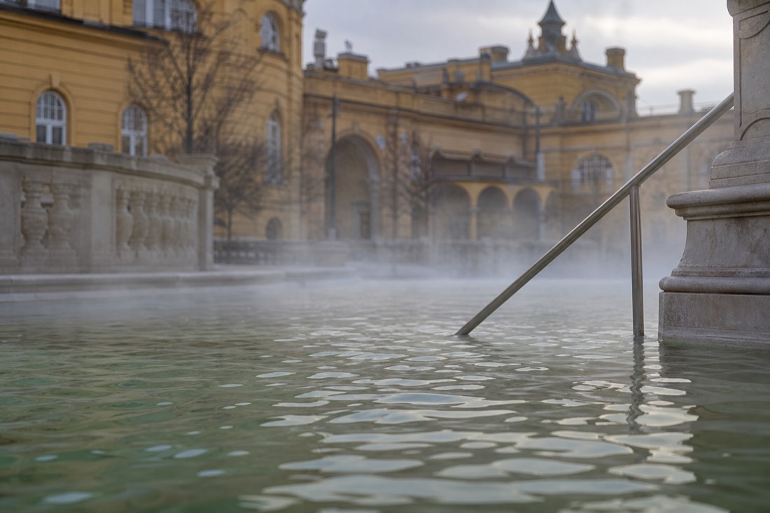 Morning steam drifting over calm thermal water in a Budapest bath courtyard