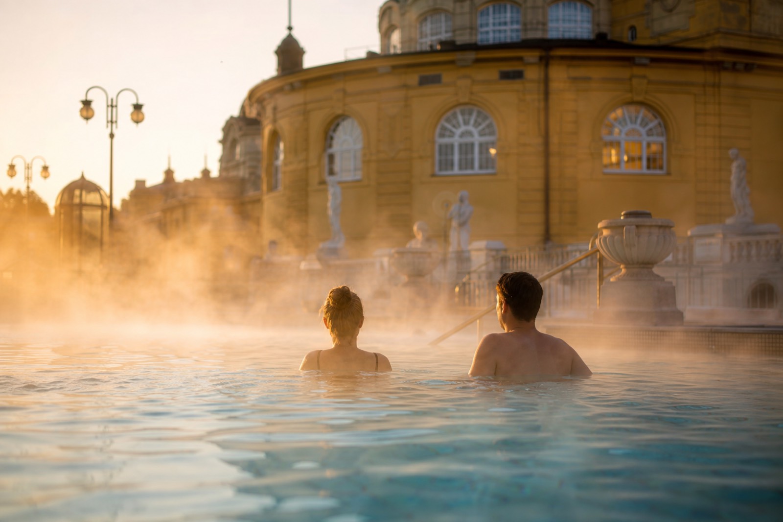 Couple relaxing in the steam of an outdoor thermal pool at a Budapest bath at sunrise