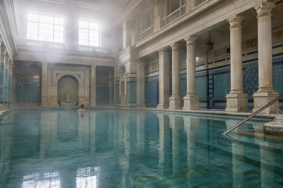 Calm indoor medicinal pool with still turquoise water and columns in a historic bathhouse hall