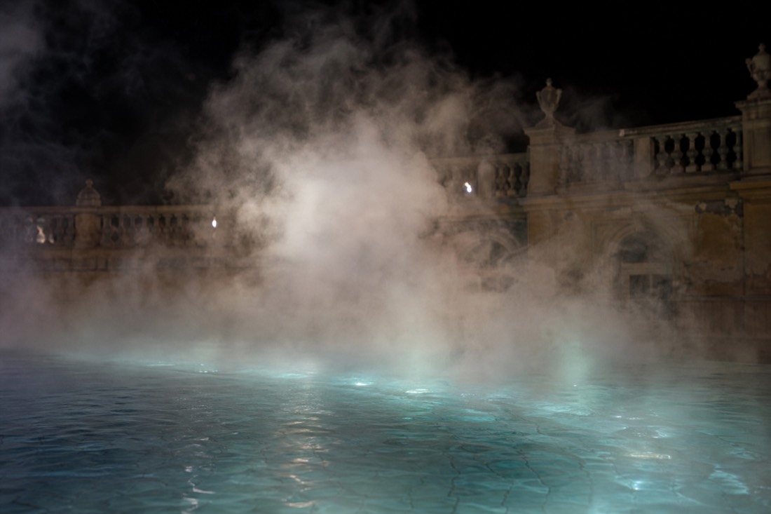 Thick steam over warm outdoor thermal water against cold night air in a Budapest bath courtyard
