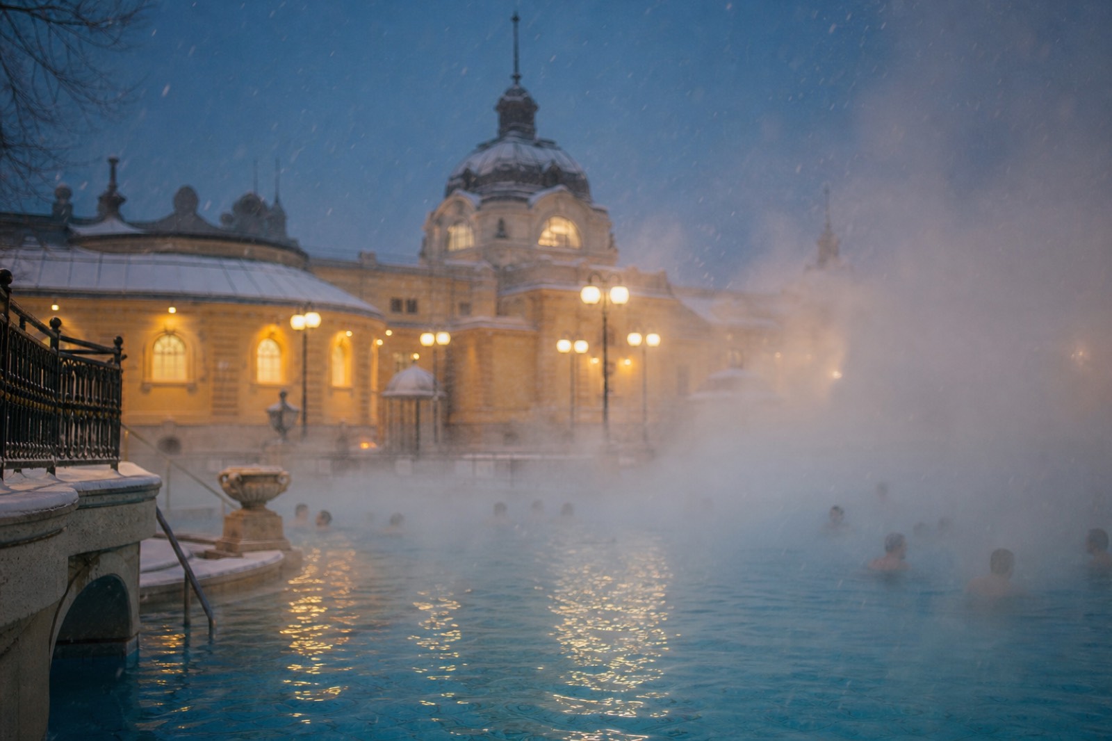 Steam rising off the outdoor thermal pool of a Budapest bath under falling snow at dusk