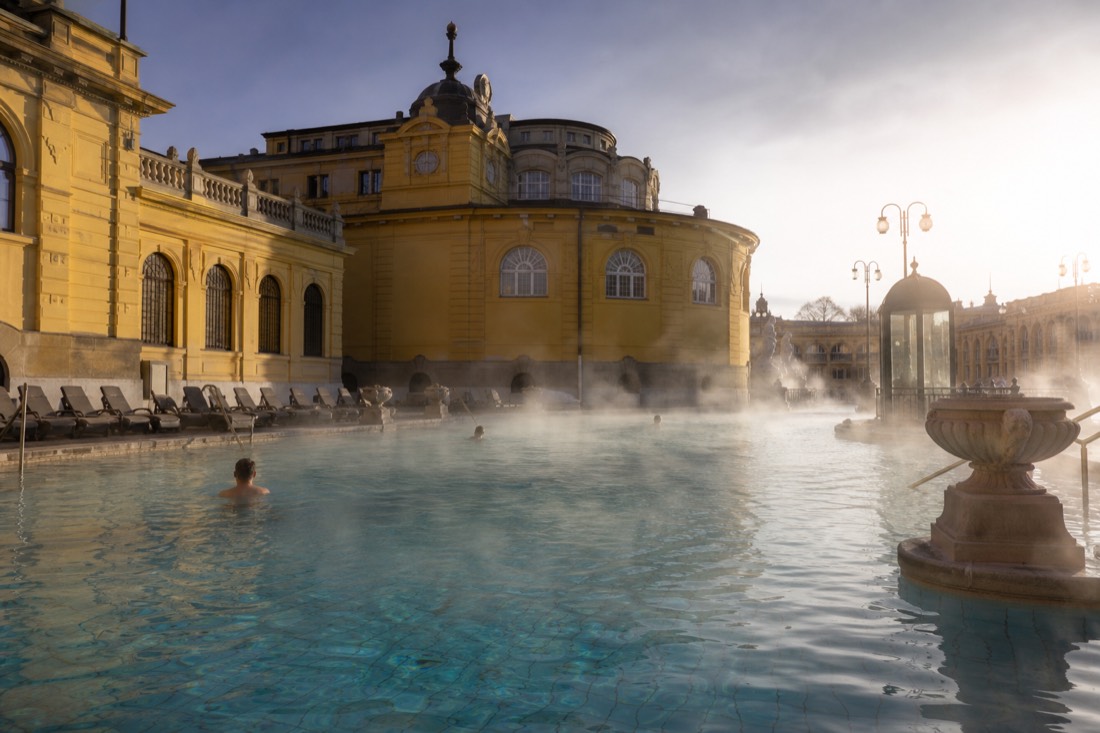 Nearly empty outdoor thermal pool at Széchenyi in early morning light with steam drifting over the water