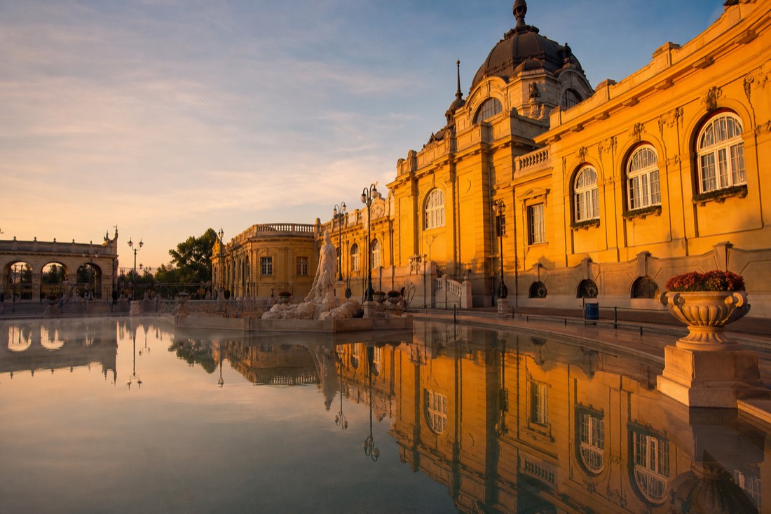 Low golden sunlight on the yellow neo-baroque facade of a grand thermal bath reflected in pool water