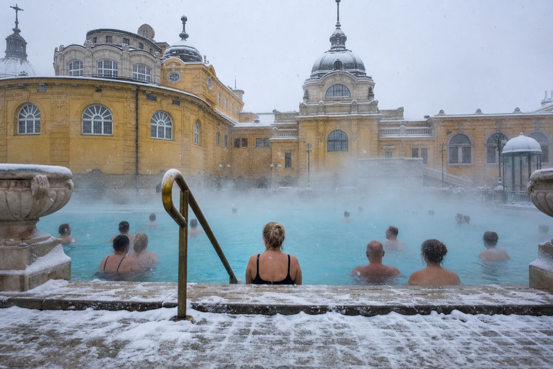 Bathers in steaming outdoor thermal water on a snowy winter day at a historic Budapest bath