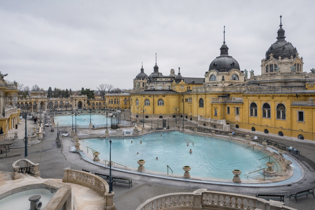 Wide view of the grand yellow courtyard of a Budapest thermal bath on a calm weekday with few bathers