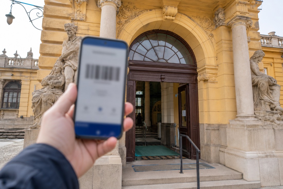 Traveller holding a phone with a mobile ticket outside the entrance arch of a Budapest thermal bath