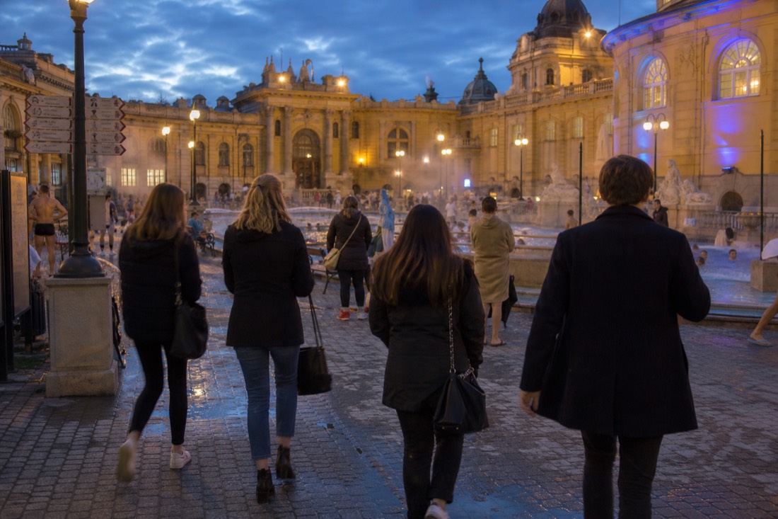 Evening crowd arriving at an ornate bath courtyard lit up for a Saturday night event in Budapest