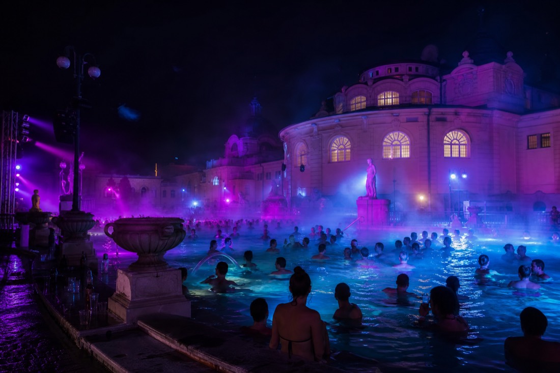 Outdoor thermal pool lit with colorful party lights at night, steam glowing above the water