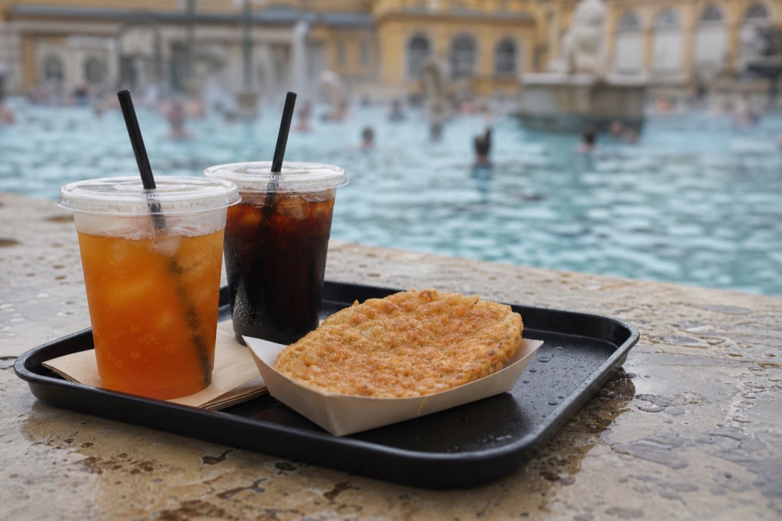 Tray with drinks and snacks on a wet poolside ledge at a busy outdoor thermal bath