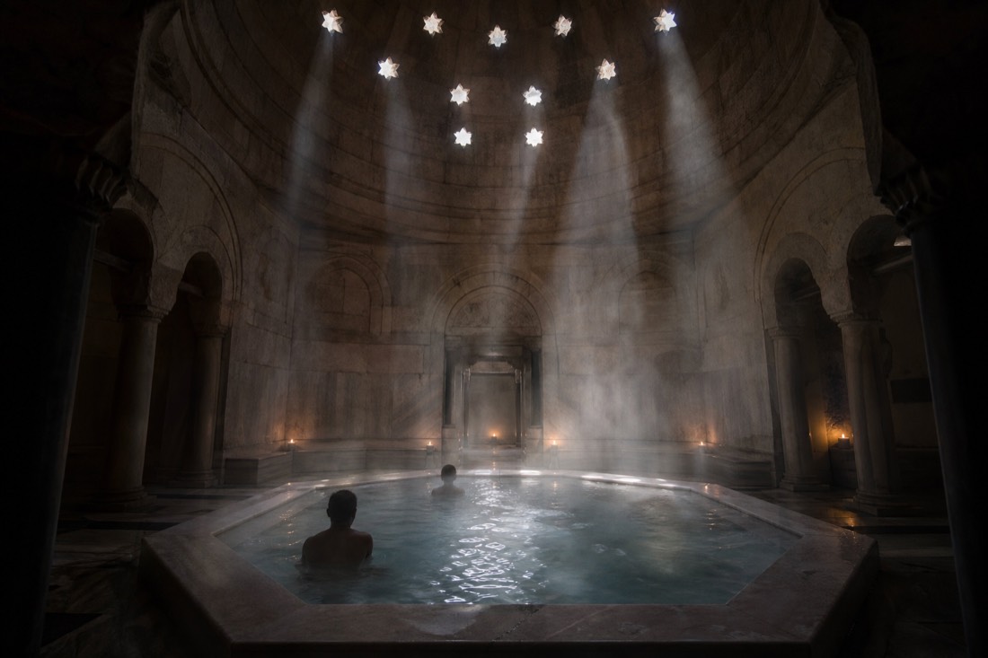 Steam drifting under the stone dome of an Ottoman-era thermal bath in Budapest lit by small skylights on a winter morning