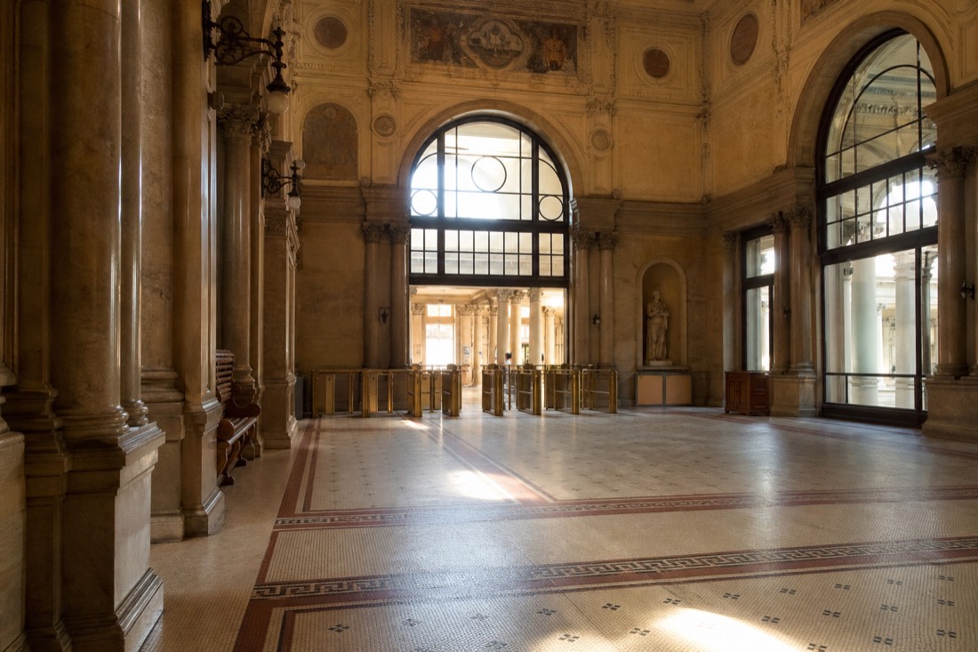 Entrance hall of a historic Budapest bath with turnstiles and warm stone arches, seen without crowds