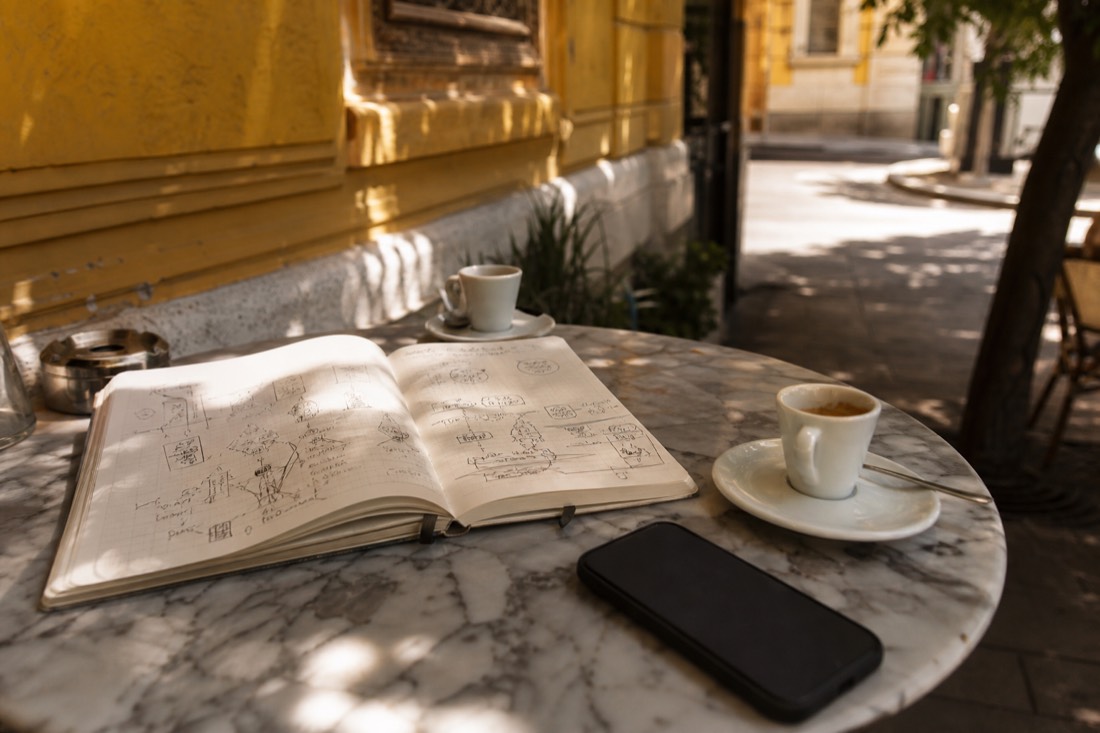 Open notebook and phone on a cafe table beside the yellow walls of a Budapest bath, trip planning scene