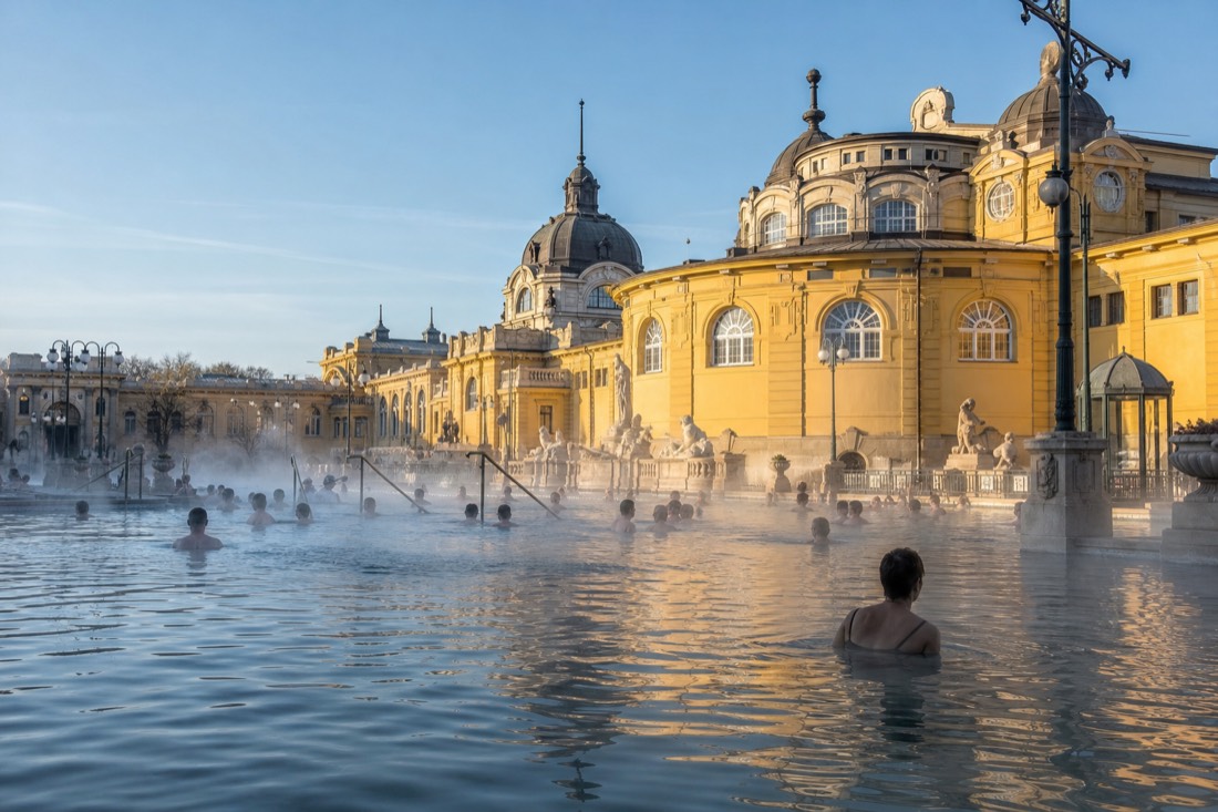 Sunlit neo-baroque courtyard of a Budapest thermal bath with bathers in the steaming outdoor pool