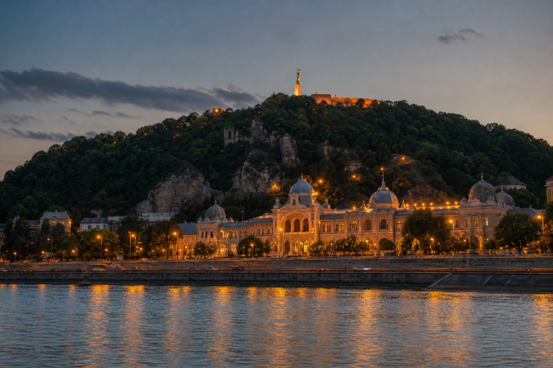 View across the Danube toward Gellért Hill at dusk with the historic bath building on the Buda bank