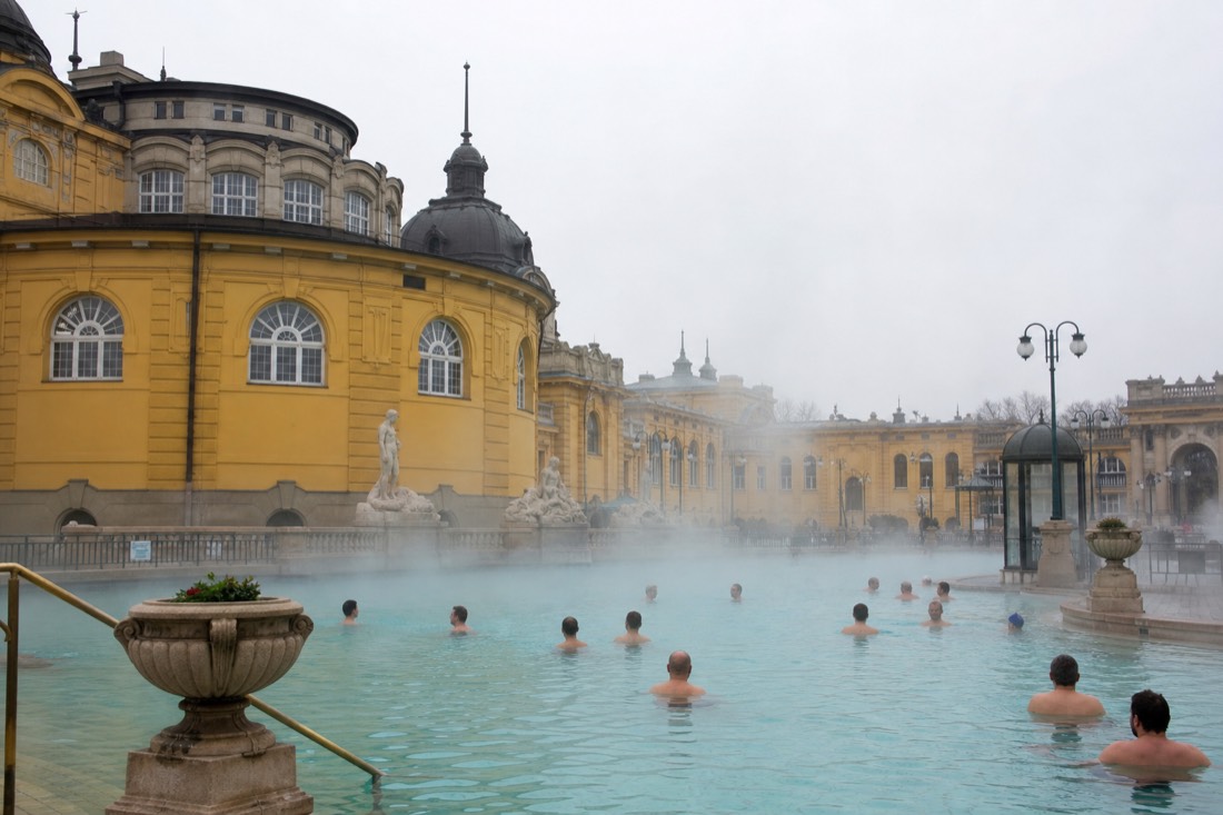 Outdoor thermal pool courtyard in Budapest with steam over warm water and grand yellow facades