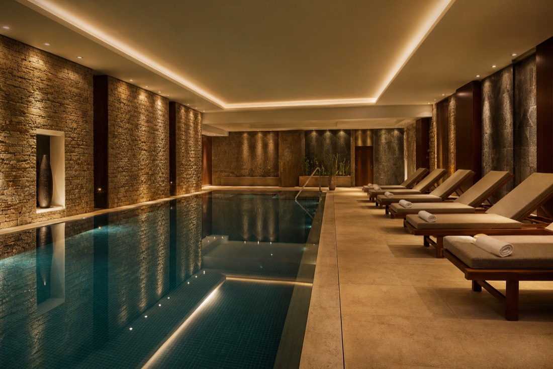 Small indoor hotel wellness pool with loungers, still water and soft light, no bathers present