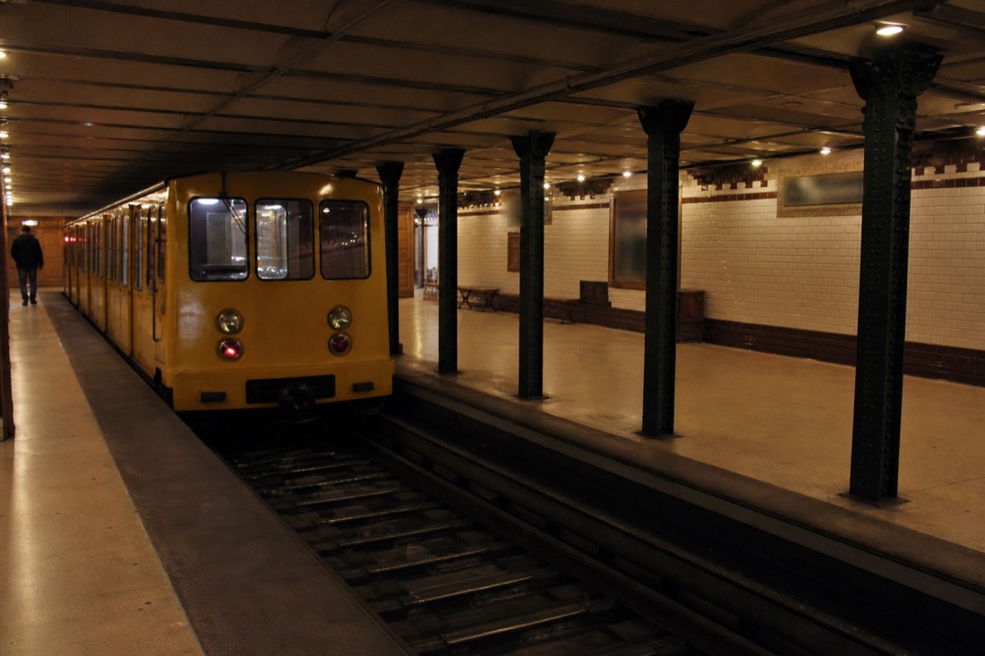 Small historic yellow metro carriage at a tiled underground station on the M1 line in Budapest