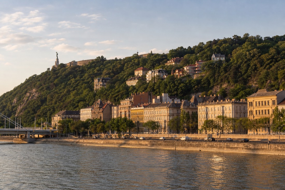 Danube riverfront on the Buda side near Gellért Hill, neighborhood streets rising behind the embankment