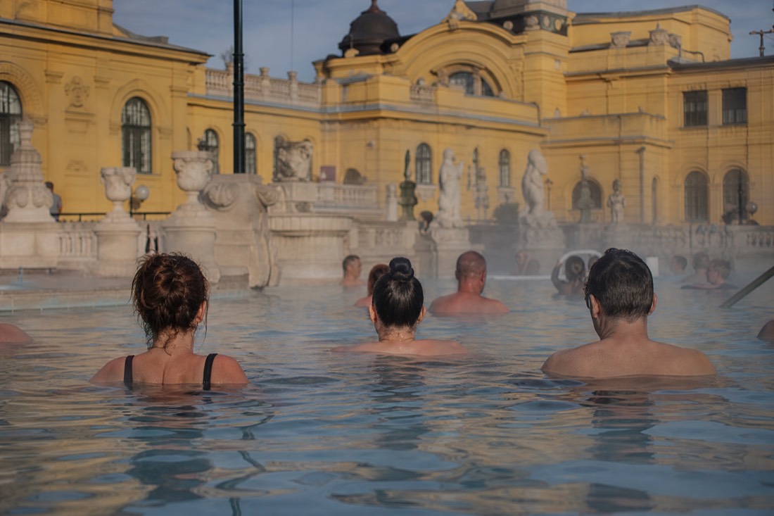 Bathers relaxing in steaming outdoor thermal water framed by neo-baroque yellow facades in Budapest
