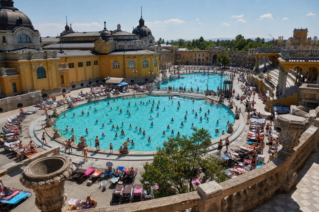 Busy summer afternoon around an outdoor bath courtyard pool with sunbathers on stone terraces