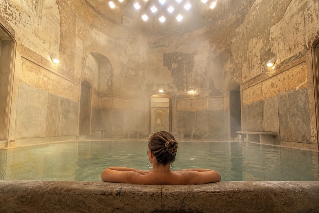 Bather resting at the edge of a warm stone pool in soft light, pacing a quiet Turkish bath session in Budapest