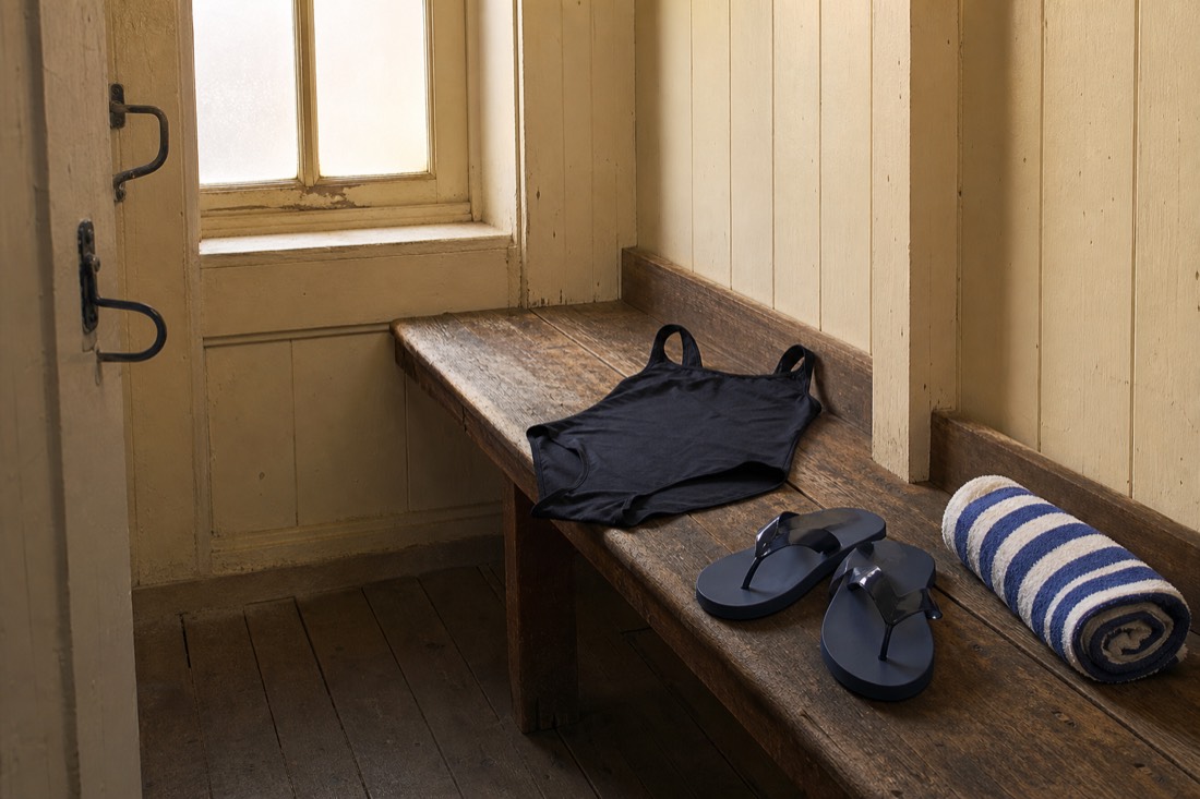 Swimsuit, flip-flops and rolled towel laid out on a bench in a Budapest bathhouse changing cabin