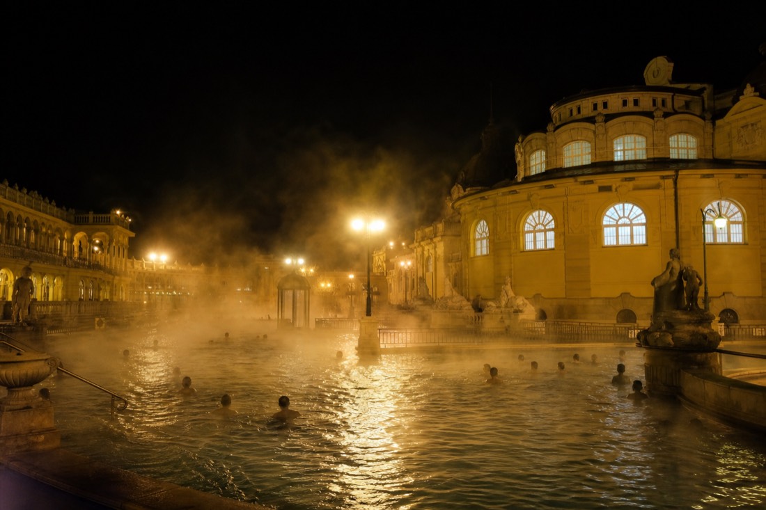 Late-evening steam rising from an outdoor thermal pool under floodlights at a Budapest bath open past dark