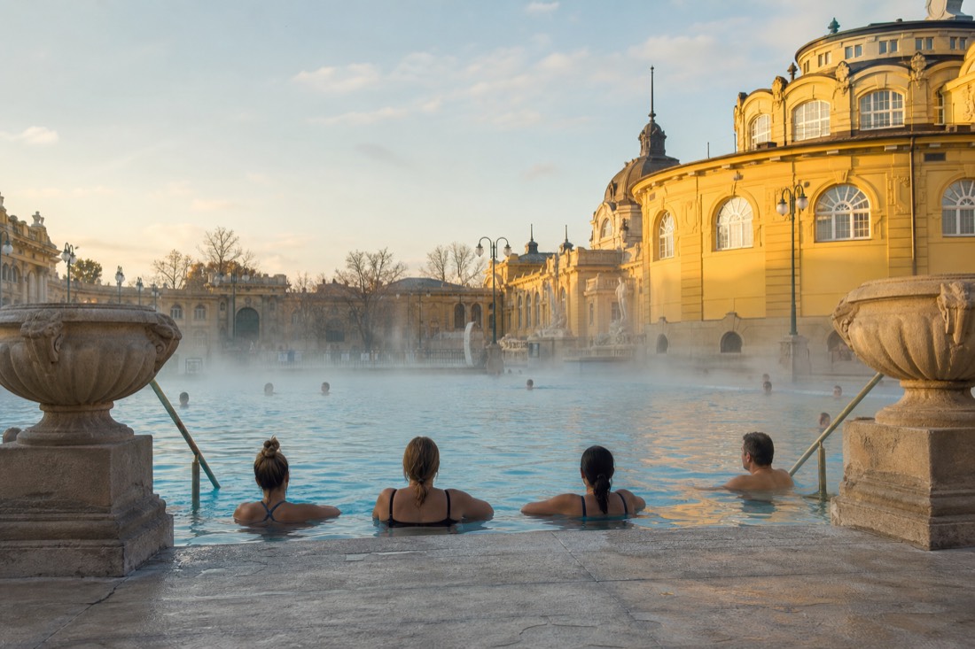 Bathers relaxing in a wide outdoor thermal pool at a grand City Park bath in Budapest