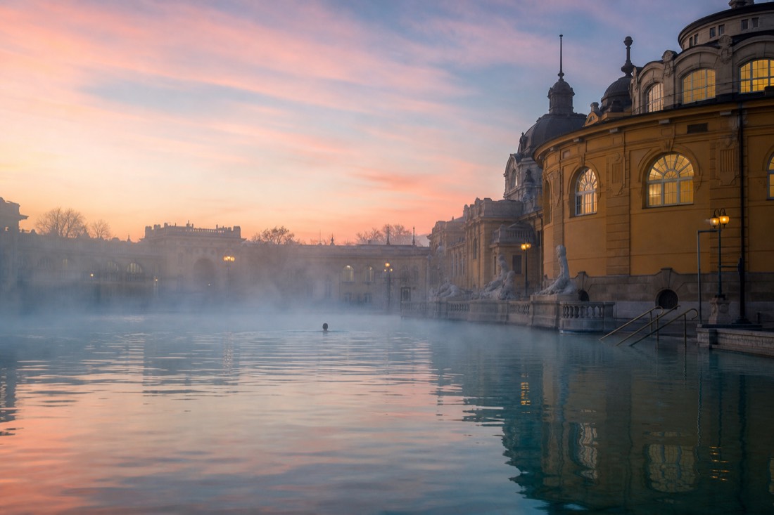 Early morning swimmer alone in a steaming outdoor pool at an open Budapest thermal bath